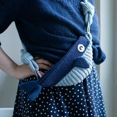 a woman wearing a blue sweater and polka dot skirt holding a knitted owl purse