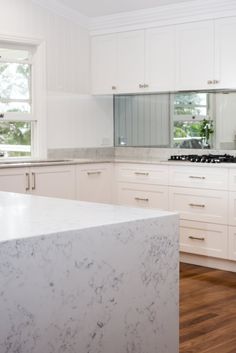 a kitchen with white cabinets and marble counter tops