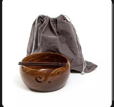 a wooden bowl with chopsticks in it next to a drawstring bag