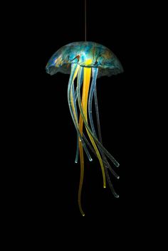 a jellyfish in the dark with yellow and blue tentacles hanging from it's head