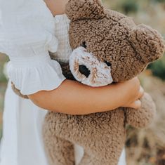 a woman holding a brown teddy bear in her arms and wearing a white dress with ruffled sleeves