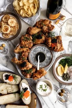 a table topped with plates and bowls filled with food next to bottles of wine on top of a marble counter