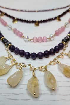 Release your inner Goddess with this gemstone and beaded statement necklace! This absolute UNIT of a necklace features lepidolite beads. Lepidolite is thought to be a calming and balancing stone, sometimes used as a stress reliever or to reduce anxiety. Lovely citrine teardrop nuggets are wire-wrapped onto a gold-plated chain. Citrine is thought to boost self-esteem and confidence levels. Pink cat eye glass beads add a bright pop of color. Next, two tiers of faceted garnet stones add a nice shimmer and sparkle. Garnet gemstones are believed to have many uses, including sparking fiery passions and bringing luck to love and relationships. What are you waiting for? Step in to your power! The shortest tier of the necklace is 18.5inches long, and the necklace has a two inch extender already in Absolute Unit, Bright Pop, Love And Relationships, Art Necklaces, Inner Goddess, Eye Glass, Beaded Statement Necklace, Garnet Stone, Pink Cat