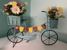 a blue bicycle with flowers in baskets on the back and welcome sign attached to it