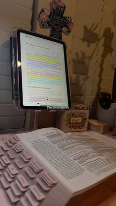 an open book sitting on top of a desk next to a computer keyboard and monitor