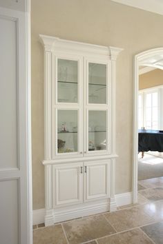 a white china cabinet with glass doors in the middle of a room next to a black piano