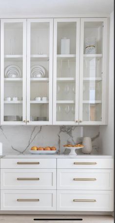 a kitchen with white cabinets and marble counter tops, gold pulls on the doors and drawers