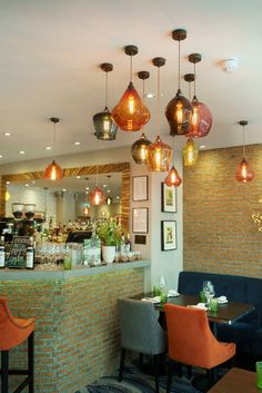 the interior of a restaurant with several lights hanging from the ceiling and colorful chairs at the bar