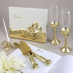 a table topped with gold colored items next to a notepad and wineglasses