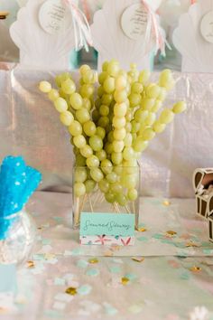 there is a small vase with grapes in it on the table next to confetti