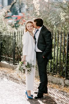 a man and woman standing next to each other in front of a black iron fence