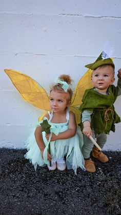 two children dressed up as tinkerbells sitting next to each other on the ground