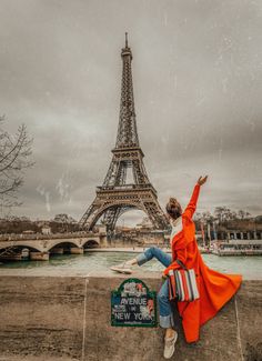 a woman sitting on the edge of a wall in front of the eiffel tower