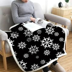 a woman sitting in a chair with a blanket on her lap and reading a book