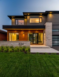 a modern house with grass in the front yard and lights on it's windows