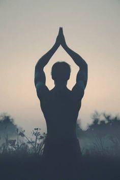 the silhouette of a man doing yoga in front of a foggy sky with his hands up