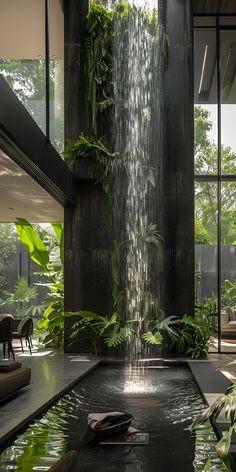 an indoor waterfall in the middle of a room with large windows and plants growing on it