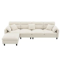 a white sectional couch with pillows on it's back and foot rests against the wall