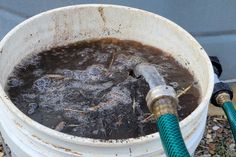 a white bucket filled with water next to a hose on top of gravel covered ground