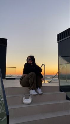 a woman sitting on the steps talking on her cell phone while looking at the sunset