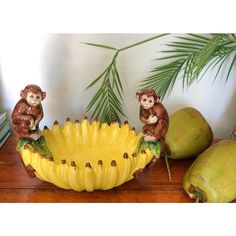 three monkey figurines sitting on top of a banana bowl next to some bananas