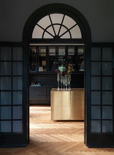 an open door leading into a kitchen with wooden floors and black walls, along with vases filled with flowers