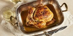 a roasted chicken in a pan with wine glasses and utensils on the side