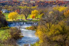 a river running through a lush green forest covered in fall foliage next to a small town