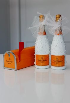 two bottles of champagne are sitting next to an orange box with a bow on it