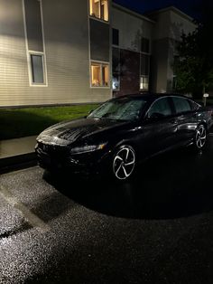 a black car parked in front of a building at night with the headlights turned on