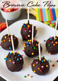 chocolate covered cake pops with sprinkles on a white plate next to a bowl of strawberries