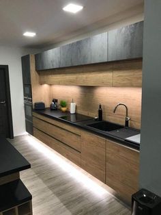 a modern kitchen with black counter tops and wooden cabinetry is lit by recessed lighting