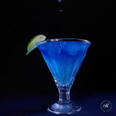 a blue cocktail with a lime wedge on the rim in front of a black background