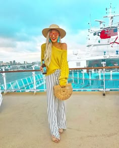 a woman standing on the deck of a cruise ship wearing striped pants and a straw hat