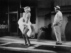 an old black and white photo of two people in front of a building, one wearing a dress