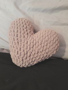 a crocheted heart pillow sitting on top of a black bed sheet in front of a white comforter