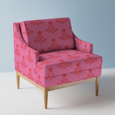 a pink chair sitting on top of a white floor next to a blue wall and wooden legs