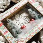 a snow scene is displayed in a box surrounded by cotton balls and other holiday decorations