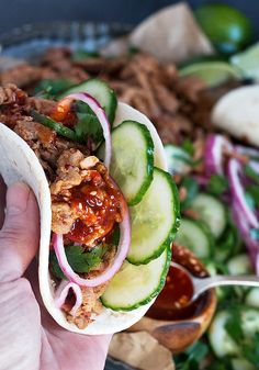 a hand holding a taco filled with meat and veggies next to a salad