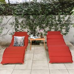 two red lounge chairs sitting next to each other in front of a plant covered wall