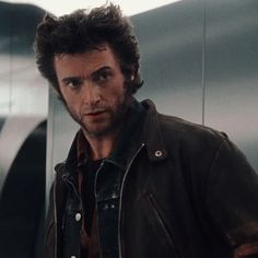 a man in a leather jacket standing next to a metal wall and looking at the camera