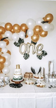 a table topped with cake and balloons in front of a one sign on the wall