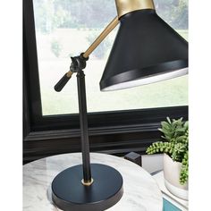 a black and gold desk lamp sitting on top of a white table next to a window