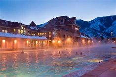 people are swimming in a large pool at night with mountains in the backgroud