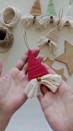 two hands are holding a piece of string with a red hat on it and some other items in the background