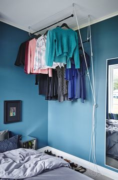 a bedroom with blue walls and clothes hanging from the rack on the wall above the bed