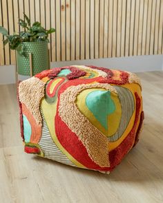 a multicolored patchwork ottoman sits on the floor next to a potted plant