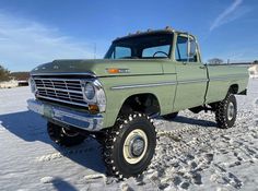 an old green pick up truck parked in the middle of snow covered ground with no one around it