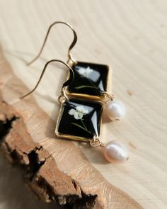 a pair of black and white square earrings with pearl beads on a piece of wood