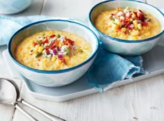 two bowls of soup on a tray with spoons and blue napkin next to it